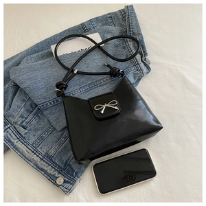 Detail of glossy black patent leather underarm bag with silver bow buckle and knotted strap
