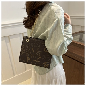 Detalle de bolso cuadrado marrón oscuro con estampados de letras y cadena de oro
