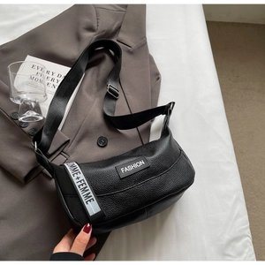 Détail du sac demi-lune noir en cuir grainé avec bandoulière large et logo tendance