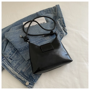Close-up of glossy black shoulder bag with knot detail on blue denim jeans