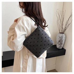 Detail of dark grey polka dot shoulder bag with bow pattern worn with a white coat