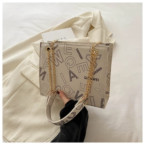 Detalle del bolso tote crema con estampado de letras y cadena dorada sobre un blazer