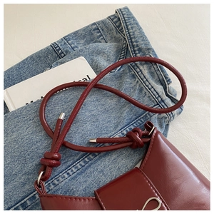 Detail of burgundy leather shoulder bag with silver bow buckle on denim background
