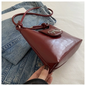 Detail of burgundy patent leather bag with silver metal bow and matching rope strap