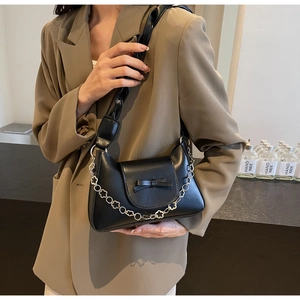 Detalle de bolso de media luna negro con cadena decorativa de flores y un lazo