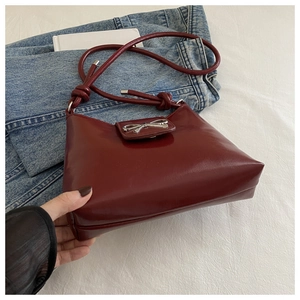 Detail of dark red glossy shoulder bag featuring a silver metal bow clasp and knot strap