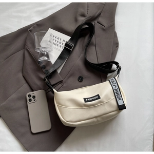 Détail du sac dumpling beige en cuir grainé avec un écusson de mode lettré