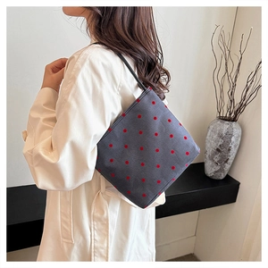 Detailed close-up of a stylish grey canvas shoulder bag with red polka dots and black handles