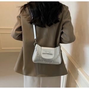 Bolso bandolera plateado con un elegante lazo y cadena metálica en una modelo
