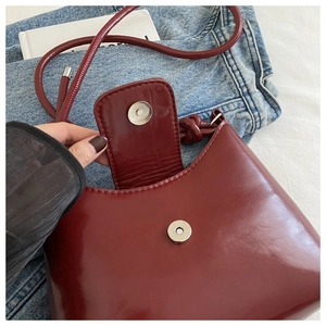 Close-up of wine red glossy PU leather bag with magnetic buckle and fine stitching