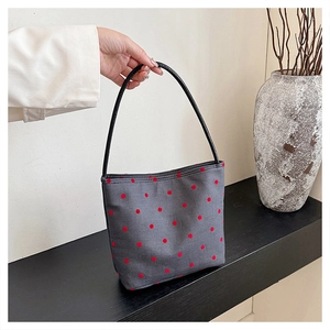 Close-up of gray canvas shoulder bag with red polka dots and elegant black handle