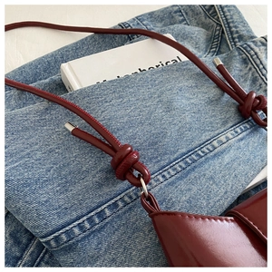 Detail of burgundy glossy leather bag with decorative knot and silver metal aglet