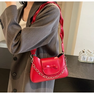 Detalle de bolso bandolera rojo con lazo y correa de cadena plateada de flores