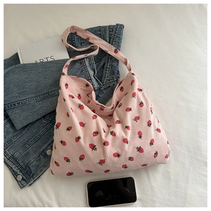 Sac hobo en velours côtelé rose à imprimé fraises à côté d'un jean et d'un livre