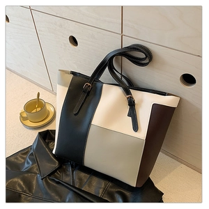 Detail of color-block tote bag with adjustable straps and gold buckles in urban setting