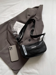 Sac bandoulière demi-lune en cuir noir grainé avec bandoulière large sur un blazer