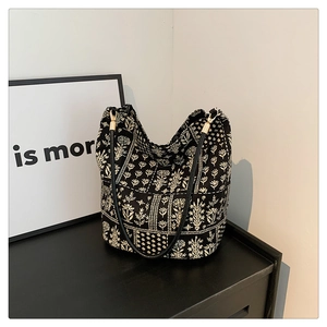 Detalle del bolso tipo cubo de lona floral con correas de cuero negro y herrajes dorados