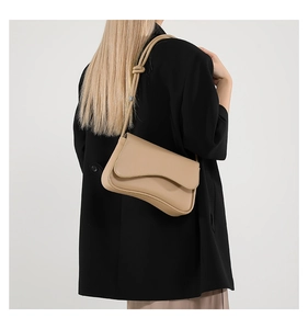 Detalle de bolso de cuero beige con base curva ondulada y correa con nudo decorativo