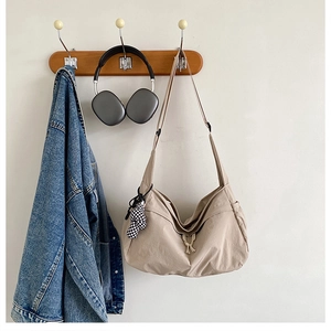 Detail van beige canvas draagtas met verstelbare riem en een geruit beer-accessoire