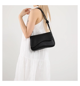 Detalle de un bolso de hombro negro minimalista que muestra el nudo decorativo en la correa