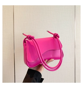 Detalle de bolso rosa intenso con solapa ondulada y correa de nudo grueso moderno