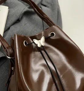 Détail du sac seau marron montrant le cordon de serrage et la boucle papillon argentée