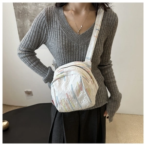 Gros plan d'un mini sac bandoulière blanc avec broderie ondulée et détails de lettres gaufrées
