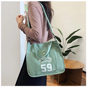 Detailed view of a green canvas tote bag featuring letter prints and a side pocket