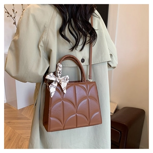 Sac bandoulière marron en cuir matelassé avec foulard en soie porté sur un trench-coat
