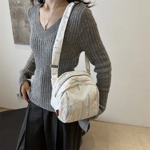 Sac bandoulière blanc avec broderie colorée et large sangle porté par un mannequin
