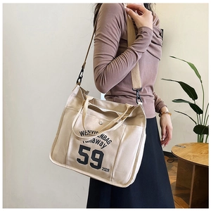 Detail of beige canvas tote bag showing front letter print and functional front pocket