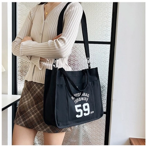 Close-up of black canvas tote bag showing white letter print and wide shoulder strap