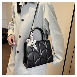 Détail d'un sac à main noir matelassé avec foulard en soie et texture cuir PU mat