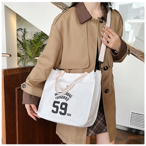 White canvas tote bag with black letter print and adjustable strap shown on a model