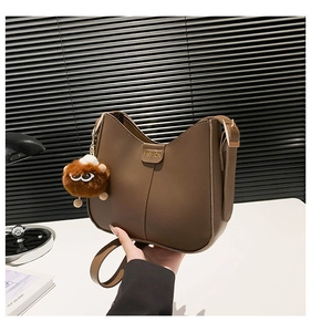 Close-up of brown faux leather bucket bag with fashion label and plush monster pendant