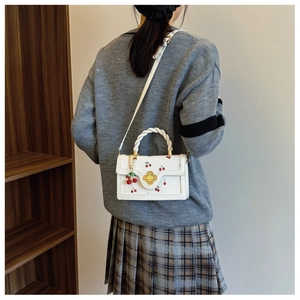 Detail van witte crossbodytas met kersenprint en gouden bloemsluiting en handvat