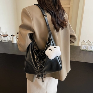Borsa tote nera minimalista con spalline incrociate e ciondolo a orsetto in un caffè