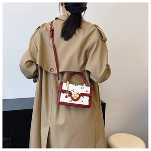 Detail van een witte crossbodytas met kersenprint en rood gevlochten handvat bij model