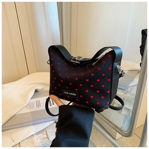 Détail du mini sac noir avec motifs de cœurs rouges, boucle argentée et poignée en cuir