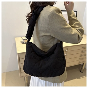 Detail of black quilted puffer tote bag featuring a large decorative bow on the strap
