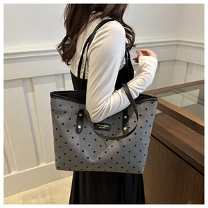 Close-up of gray polka dot tote bag with black straps and fashion brand logo patch