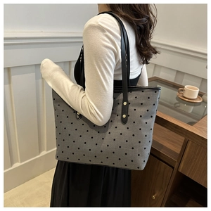 Side view of a large grey polka dot tote bag with black rivet straps on a model