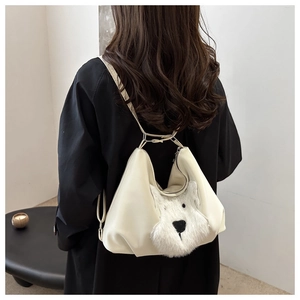 Close-up of cream white shoulder bag featuring a cute plush puppy patch on smooth faux leather