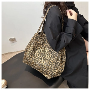 Detail of a large leopard print tote bag in canvas fabric worn over a black trench coat