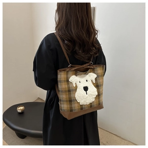 Rear view of a model wearing the brown plaid tote bag with cute plush dog patch detail