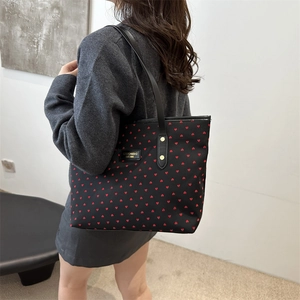 Chic black tote bag with red heart patterns and gold studs shown on a model