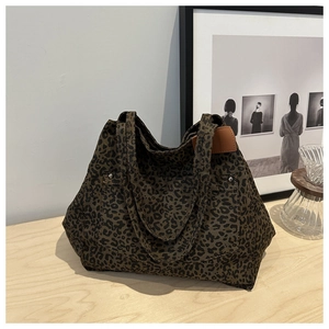 Detail of leopard print tote bag on wooden table with brown leather strap and metal buckle