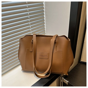 Dettaglio della borsa tote in pelle marrone con logo inciso e luce soffusa dalla finestra