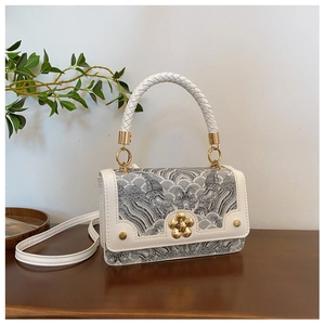 Close-up of white leather handbag featuring traditional embroidery and golden flower lock