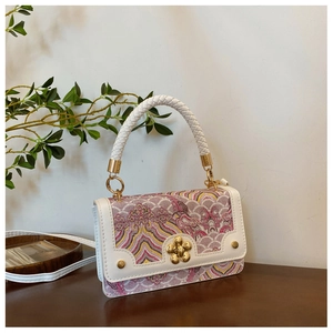 Detail of vintage square bag showing white woven handle and golden floral clasp on floral fabric
